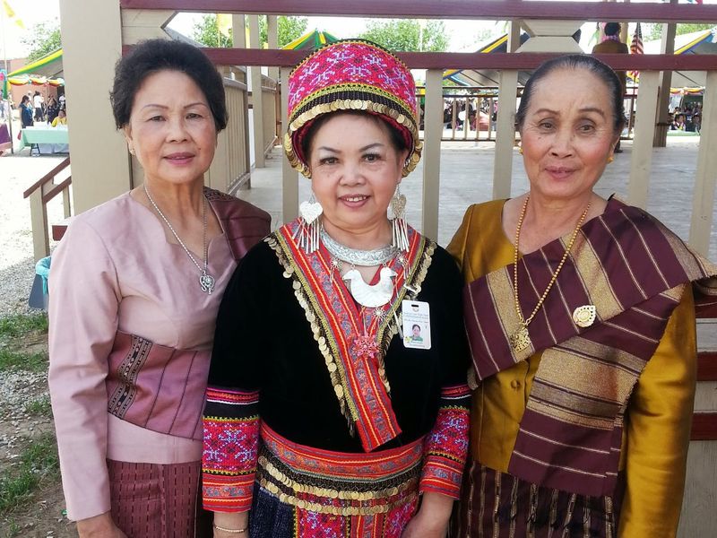 Three women in traditional Lao and Hmong dress at a community celebration