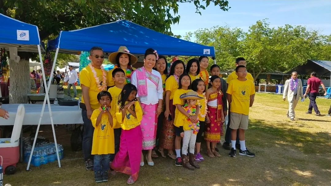 A large group of children and adults in matching yellow T-shirts and traditional dress at an outdoor community event