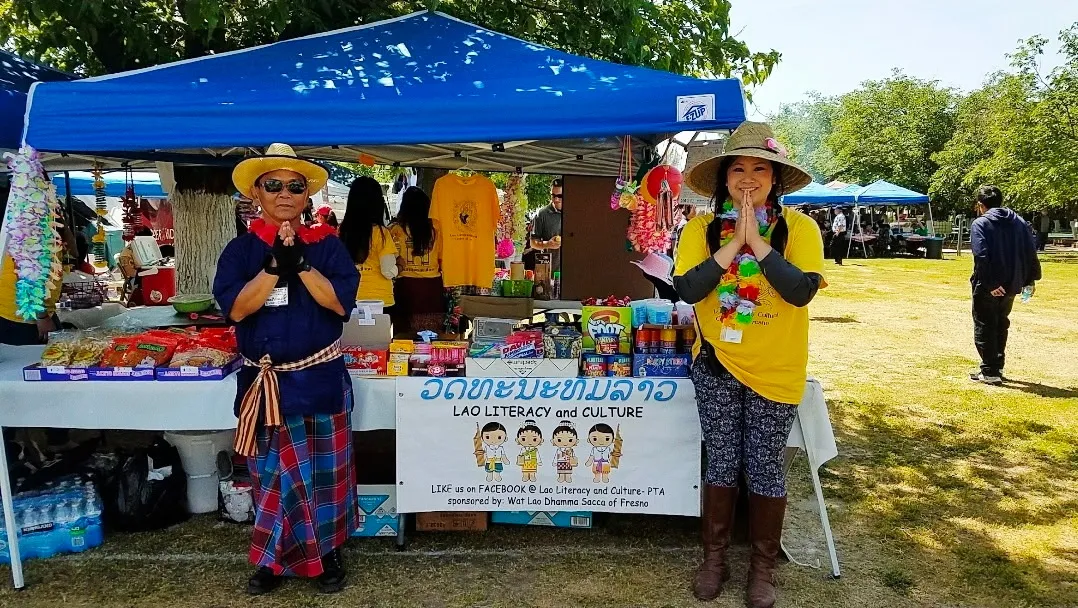 Two volunteers greet visitors at a Lao Literacy and Culture booth at an outdoor festival
