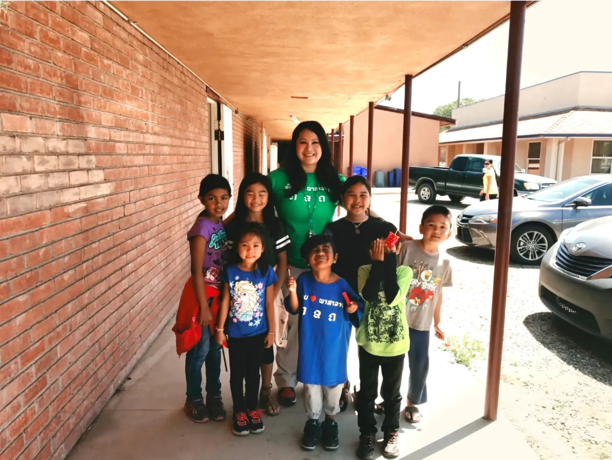 A teacher in a green shirt with a group of smiling young students outside a school