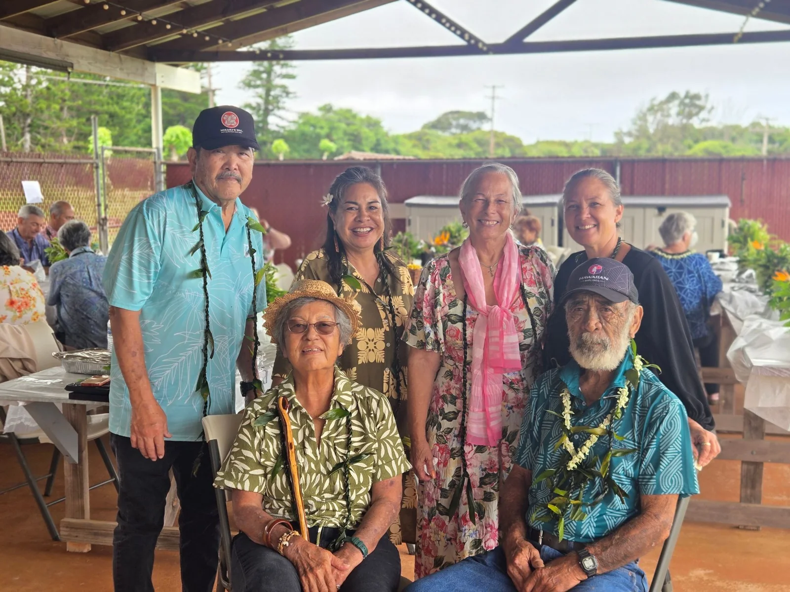 Six church members wearing lei, gathered under the pavilion at the centennial celebration.